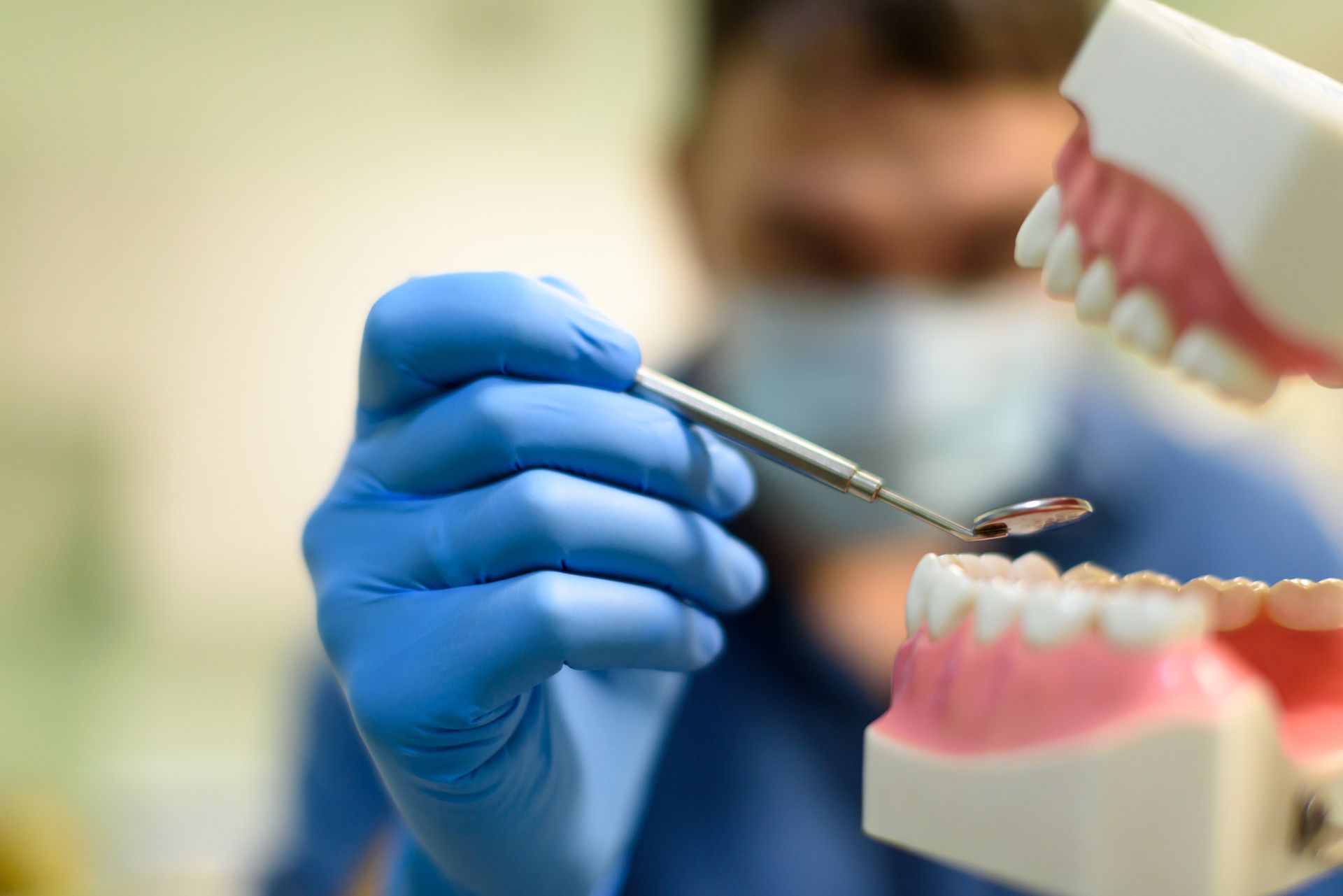 Un dentista con guantes y mascarilla azules examina una maqueta de dientes con un espejo.