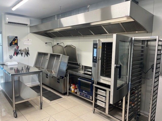 Une cuisine commerciale professionnelle équipée de tables de préparation en acier inoxydable, de friteuses industrielles, d'un four à convection et d'un chariot.