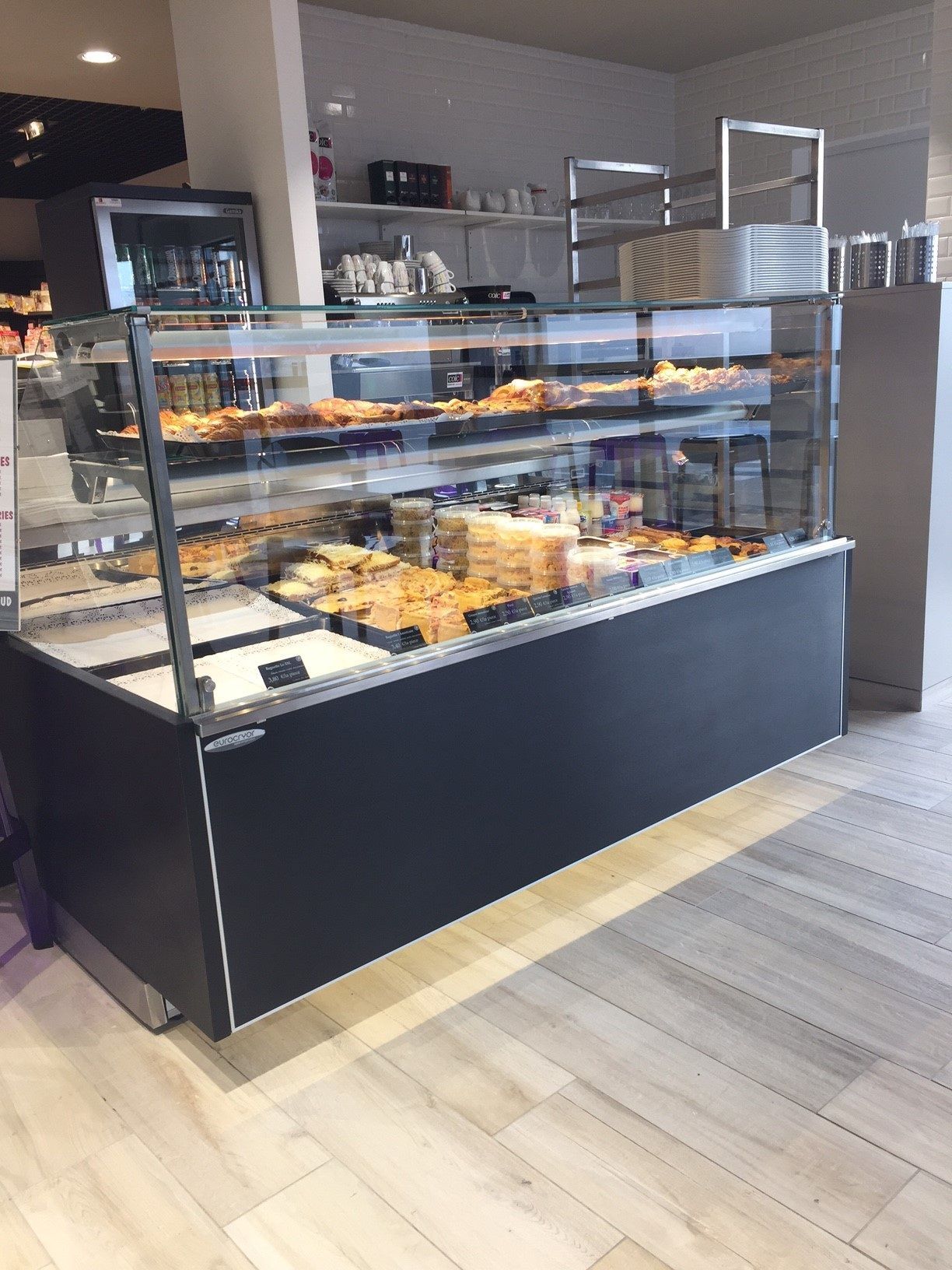 Une vitrine de boulangerie noire, à façade vitrée, remplie de pâtisseries assorties, située dans une boutique moderne au sol carrelé.