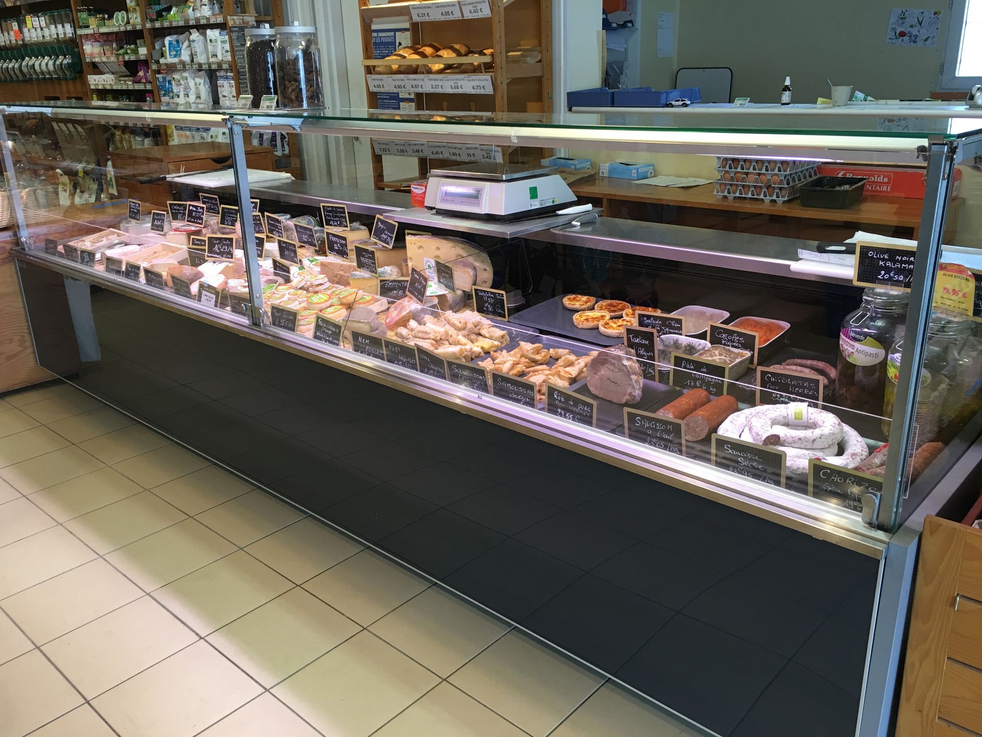 Une vitrine réfrigérée de charcuterie dans une épicerie, garnie de diverses viandes, fromages et produits alimentaires préparés.