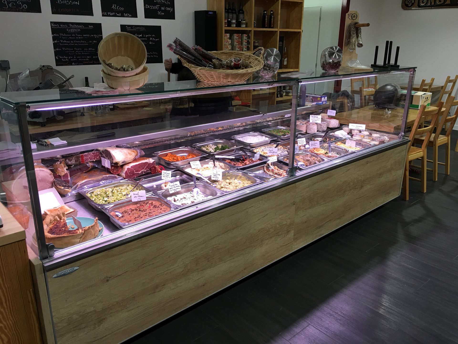 Une vitrine réfrigérée dans une épicerie fine, remplie de viandes assorties et de plats préparés, avec des côtés en panneaux de bois.