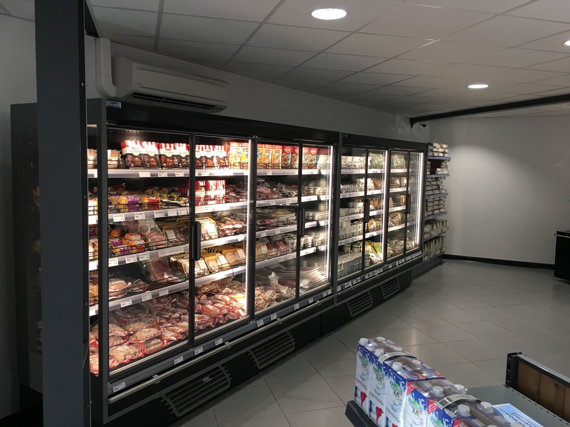 Une grande vitrine réfrigérée commerciale à plusieurs portes, remplie de produits alimentaires, dans un magasin moderne et lumineux.