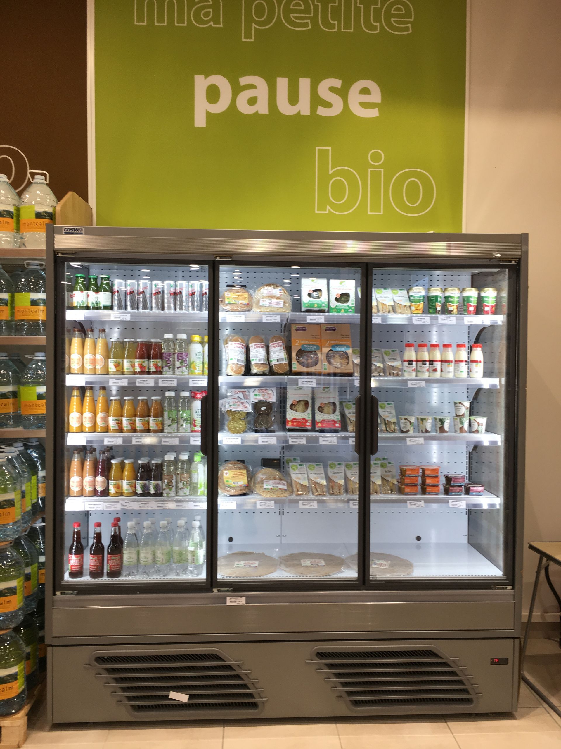 Une vitrine réfrigérée à trois portes dans une épicerie, portant une pancarte verte indiquant petite pause bio