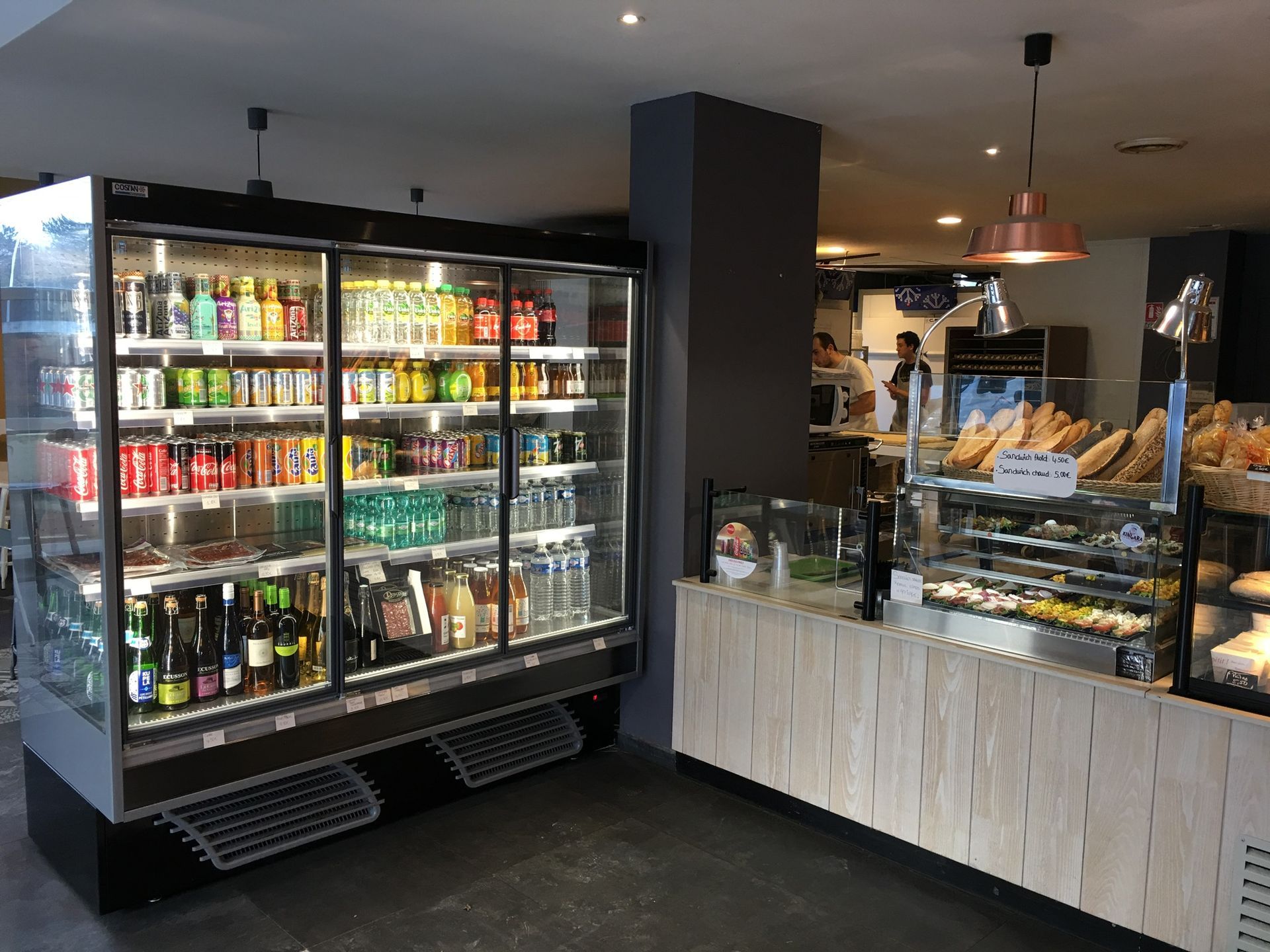 L'intérieur lumineux d'un café présente une grande vitrine réfrigérée pour les boissons à côté d'un comptoir en bois pour la restauration.
