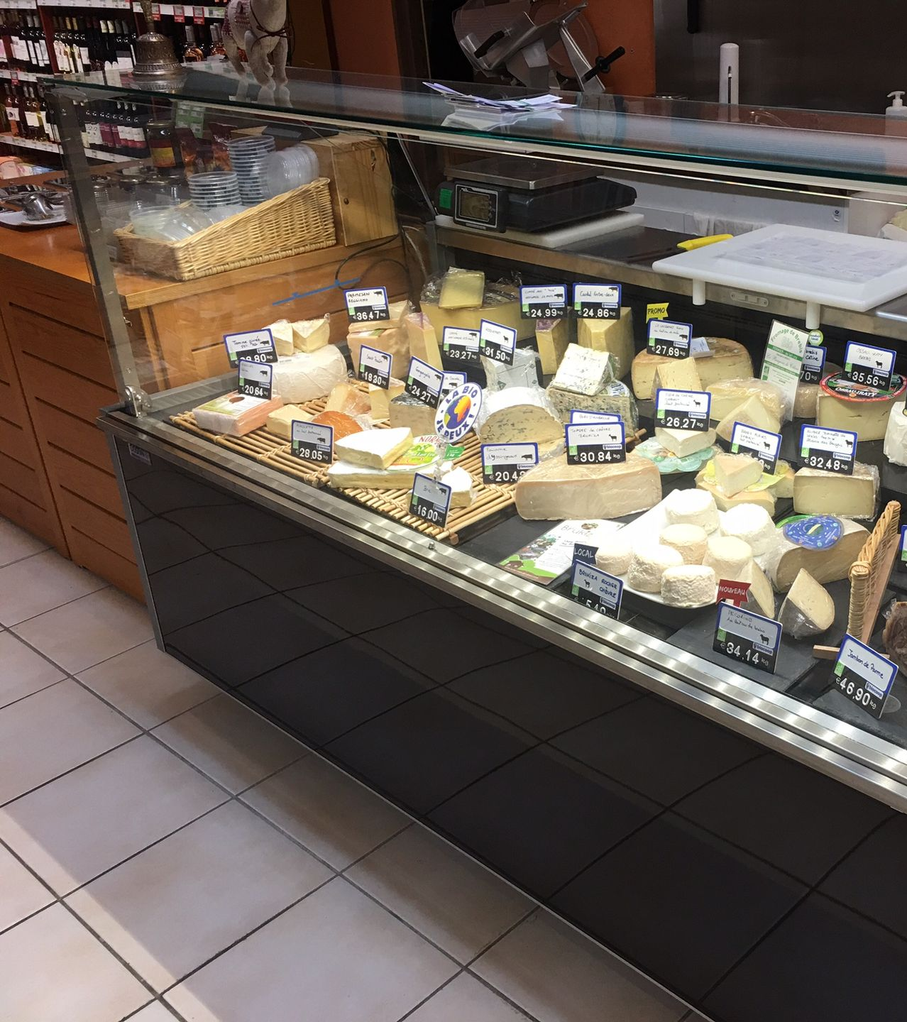 Une vitrine réfrigérée remplie d'une grande variété de fromages artisanaux, chacun étiqueté avec un petit prix.