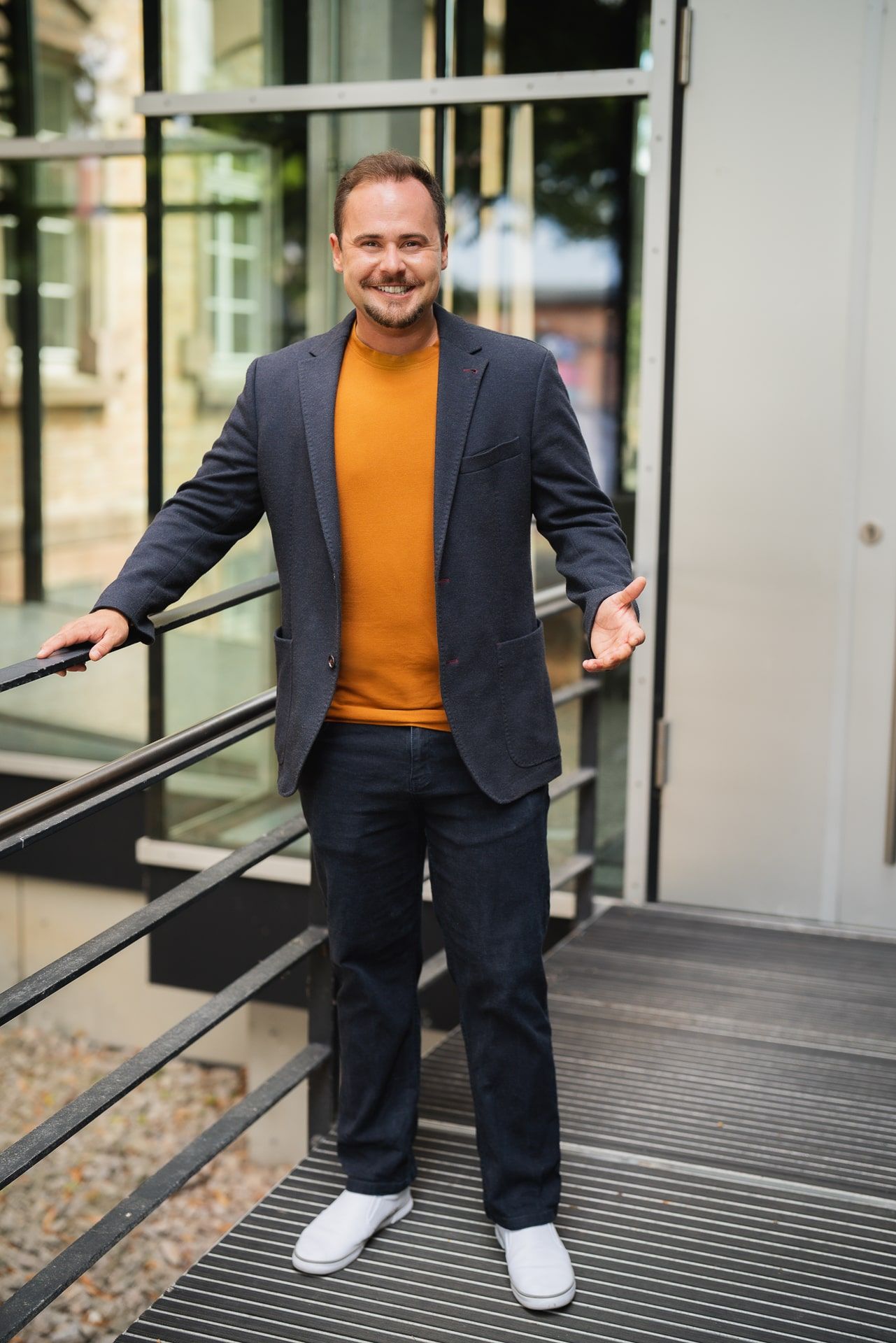 Ein Mann in Anzug und orangefarbenem Pullover steht auf einer Treppe vor einem Gebäude .