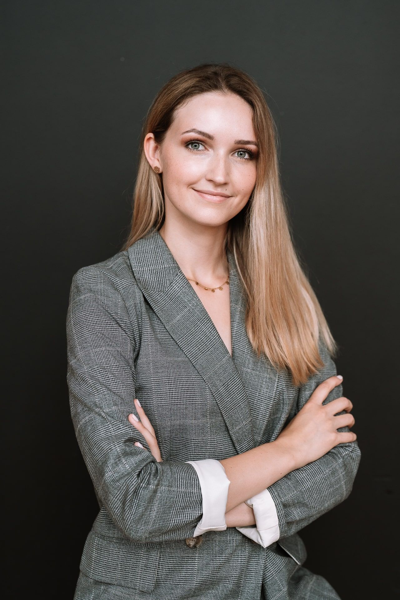 Eine Frau in einem Anzug steht mit ihren Armen gefaltet und lächelt .