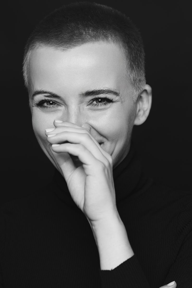 Ein Schwarzweißfoto einer Frau mit sehr kurzen Haaren, die ihren Mund mit der Hand bedeckt.
