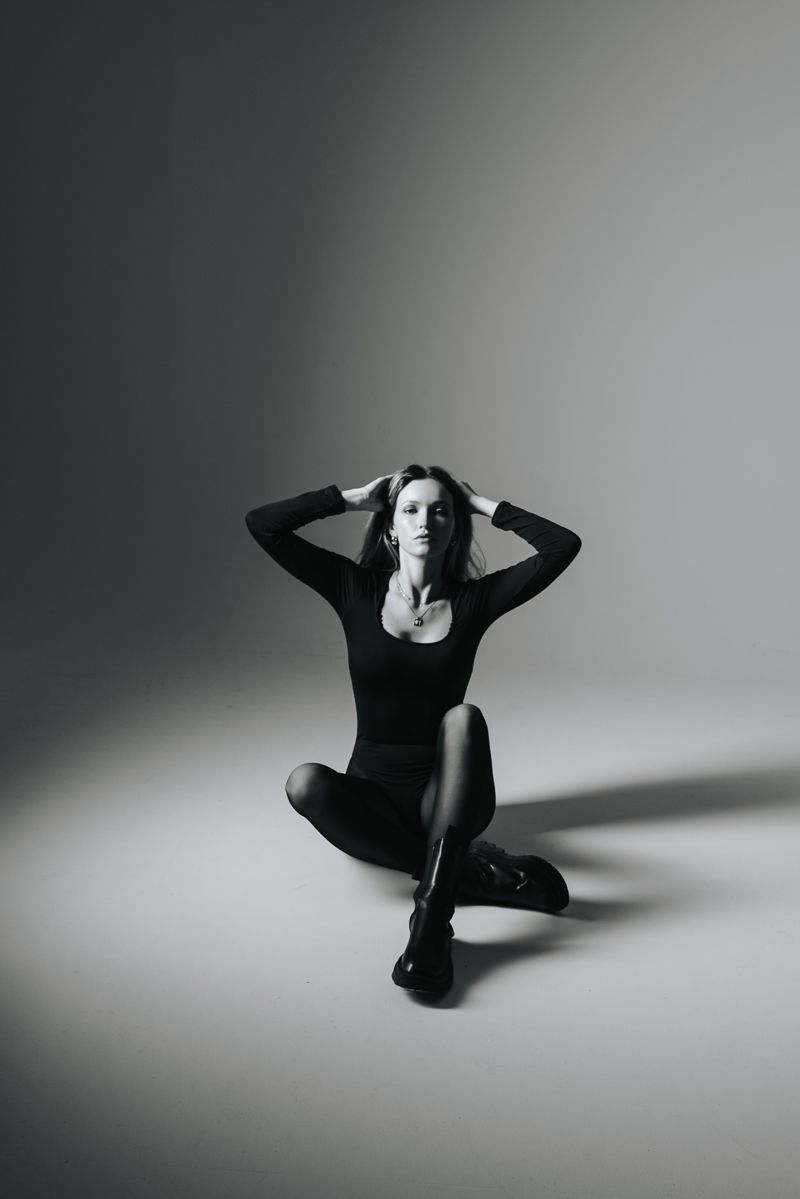 Ein Schwarzweißfoto einer Frau, die mit übereinandergeschlagenen Beinen auf dem Boden sitzt.