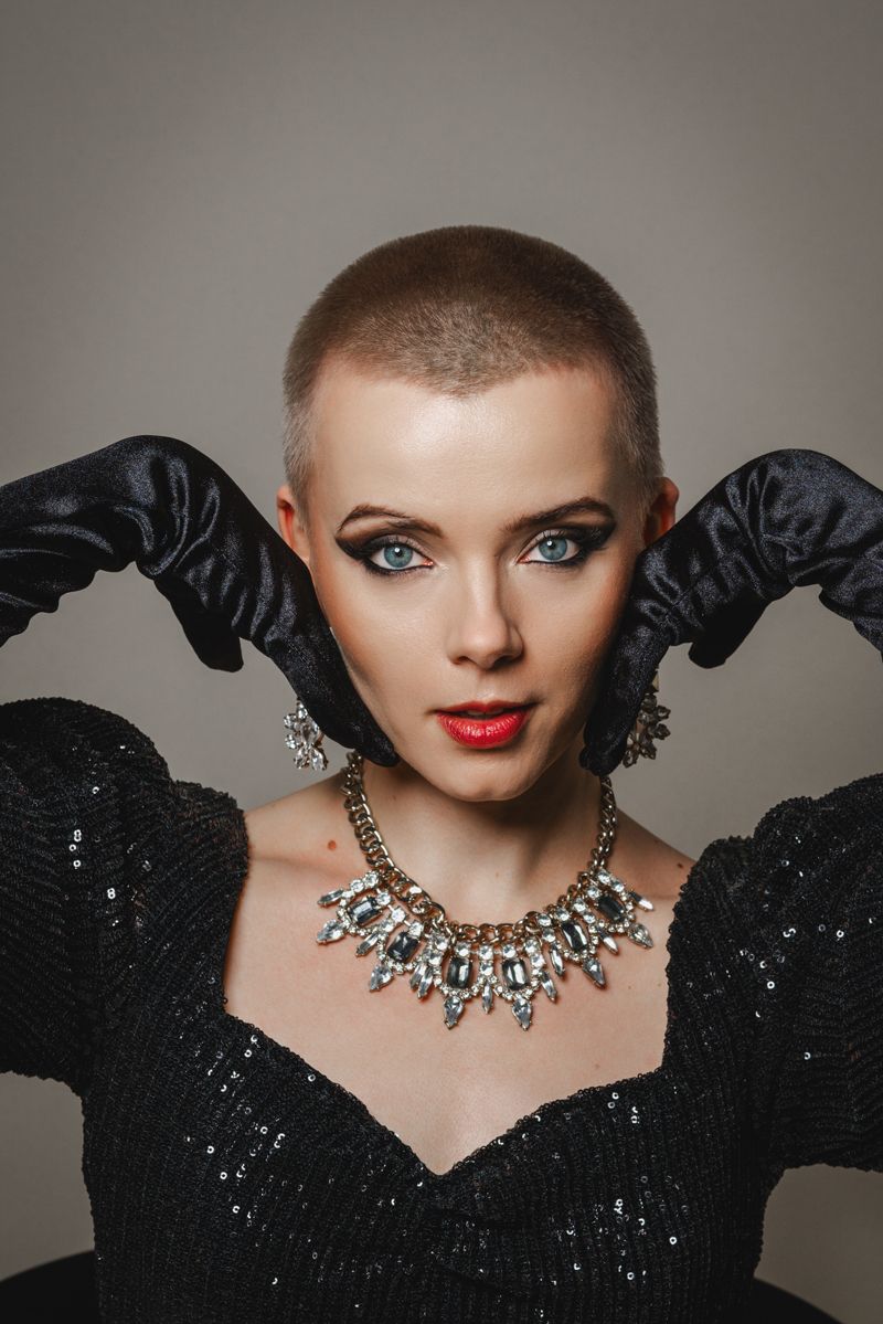 Eine Frau mit rasiertem Kopf trägt ein schwarzes Kleid und eine Halskette.