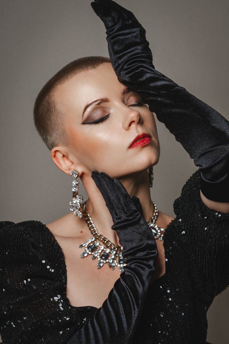 Eine Frau mit sehr kurzem Haarschnitt trägt schwarze Handschuhe und eine Halskette.