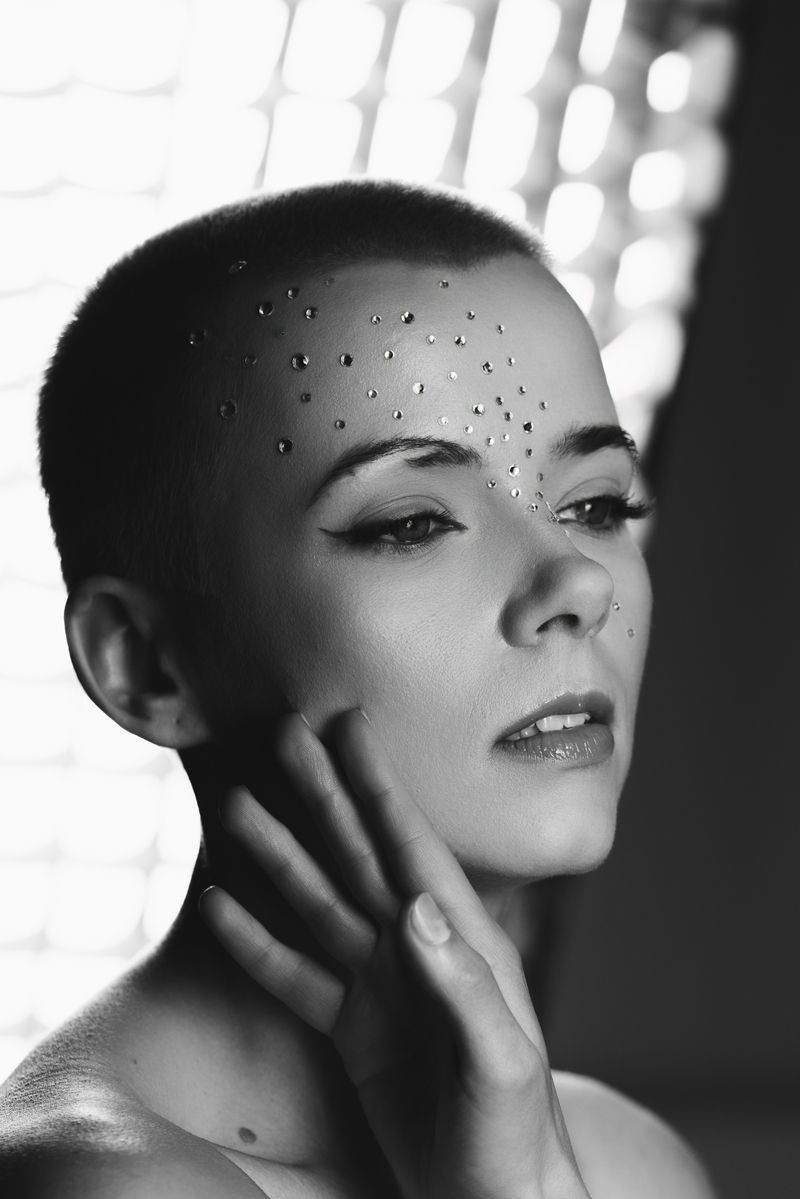 Ein Schwarzweißfoto einer Frau mit rasiertem Kopf und Strasssteinen im Gesicht.