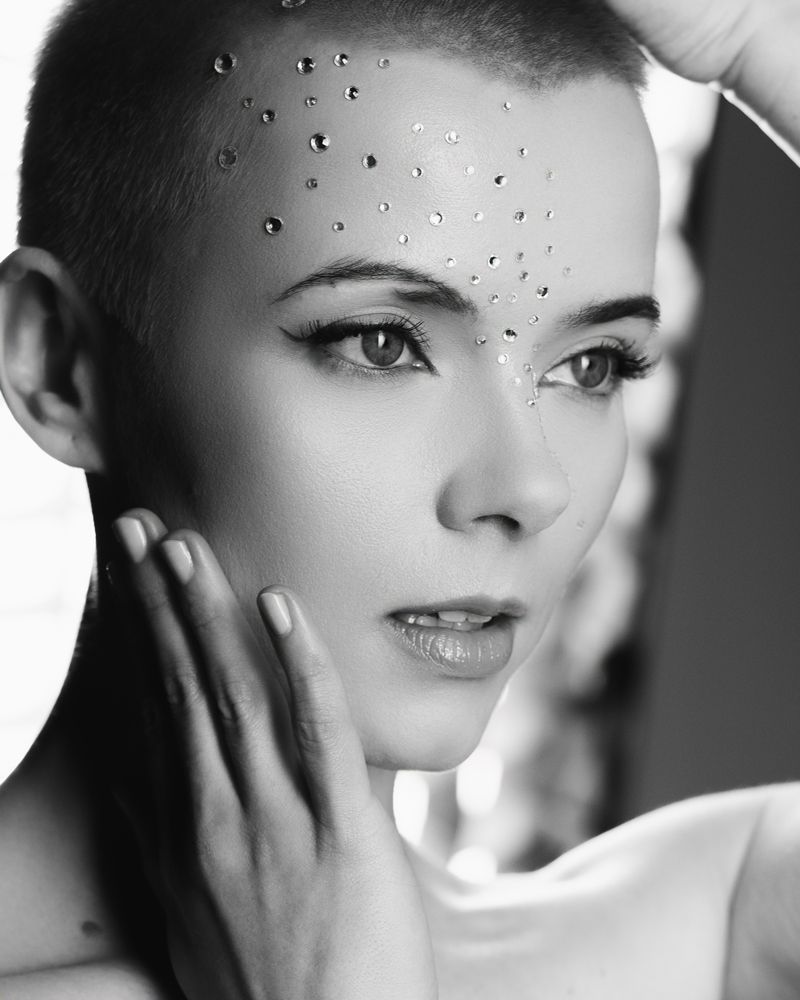 Eine Frau mit rasiertem Kopf hat Strasssteine auf der Stirn.