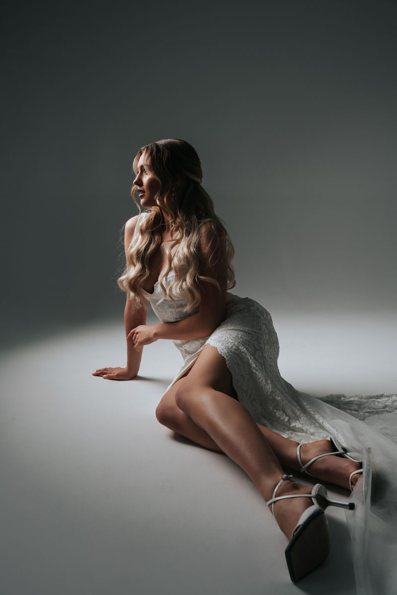 Eine Frau in einem weißen Kleid sitzt mit übereinandergeschlagenen Beinen auf dem Boden.