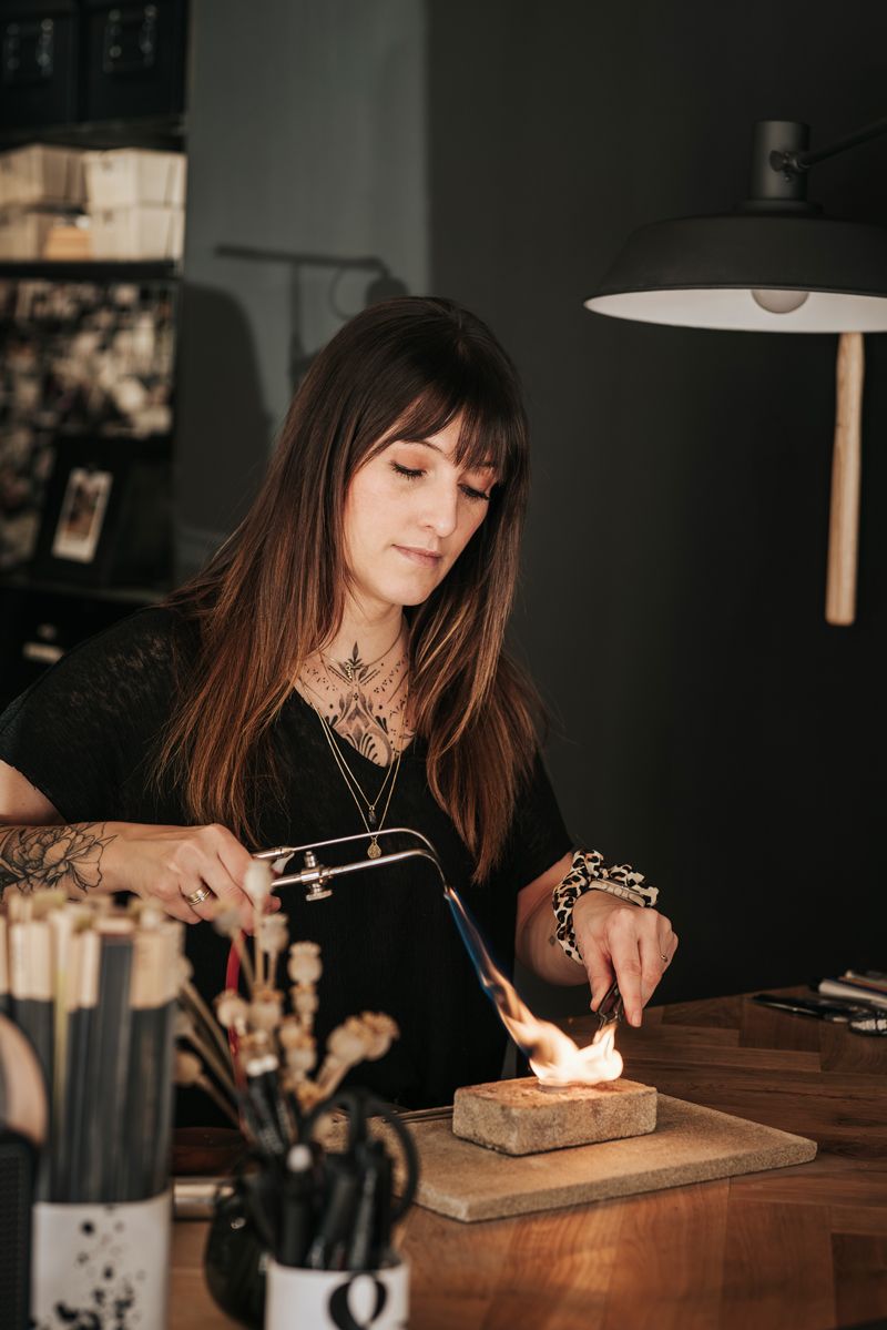 Eine Frau bearbeitet ein Stück Metall mit einem Brenner.