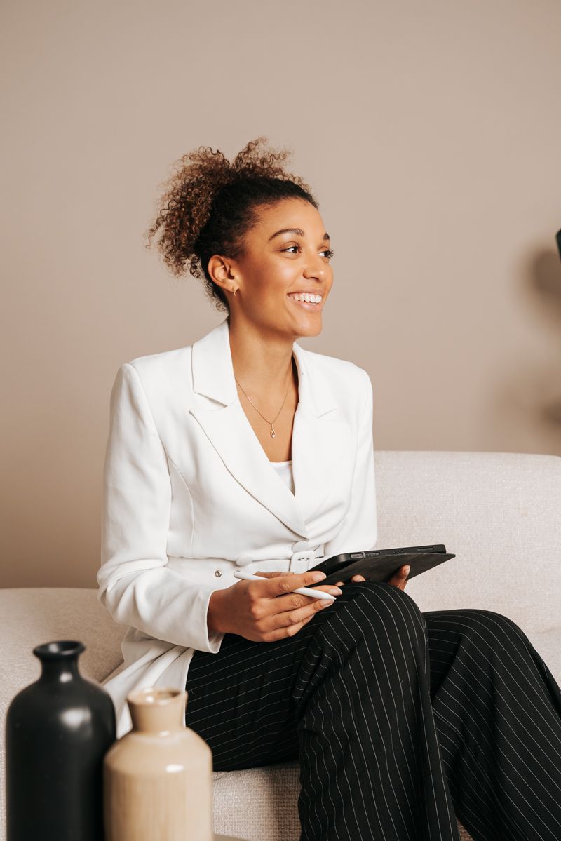 Eine Frau sitzt lächelnd auf einem Sofa, hält ein Klemmbrett in der Hand.