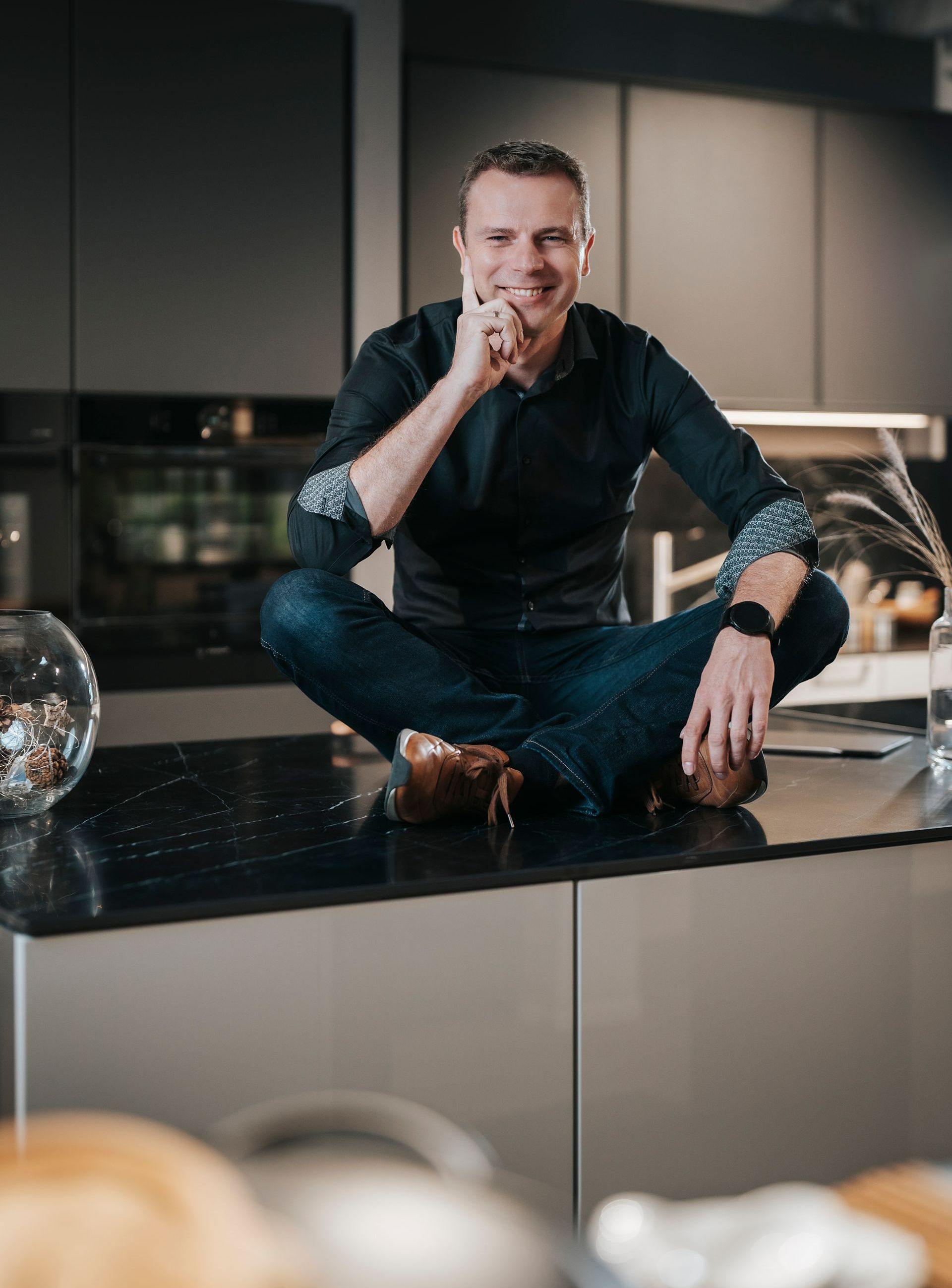 Ein Mann sitzt mit überkreuzten Beinen auf einer Küchentheke.