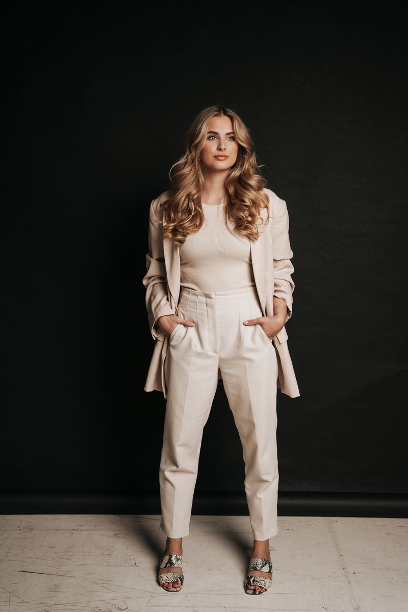 Eine Frau in einem weißen Anzug steht mit den Händen in den Taschen da.
