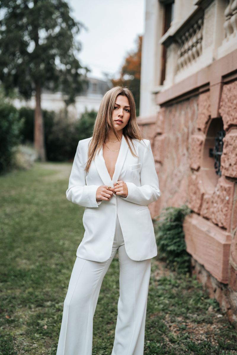 Eine Frau in einem weißen Anzug steht vor einem Gebäude.