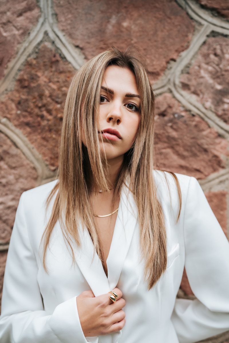 Eine Frau in einem weißen Anzug steht vor einer Steinmauer.