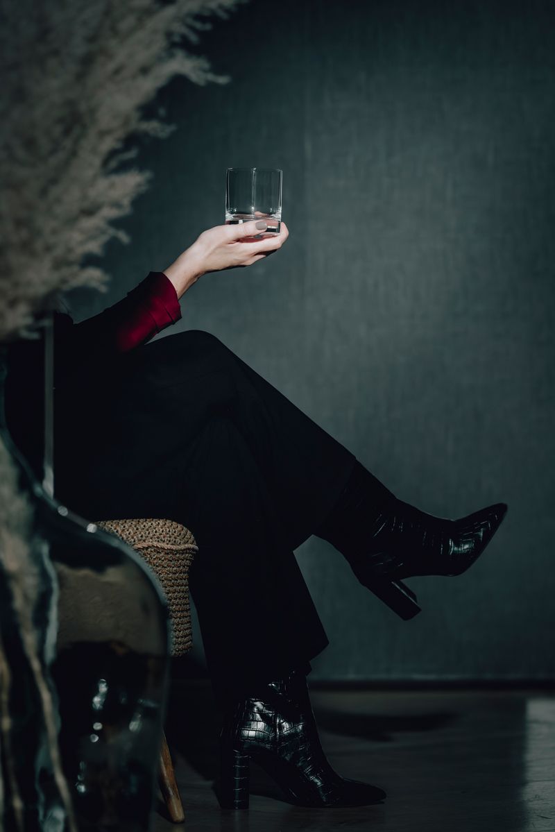 Eine Frau sitzt auf einem Stuhl und hält ein Glas Whiskey in der Hand.