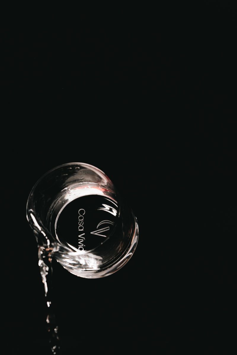 Vor einem schwarzen Hintergrund wird ein Glas Wasser in einen Messbecher gegossen.