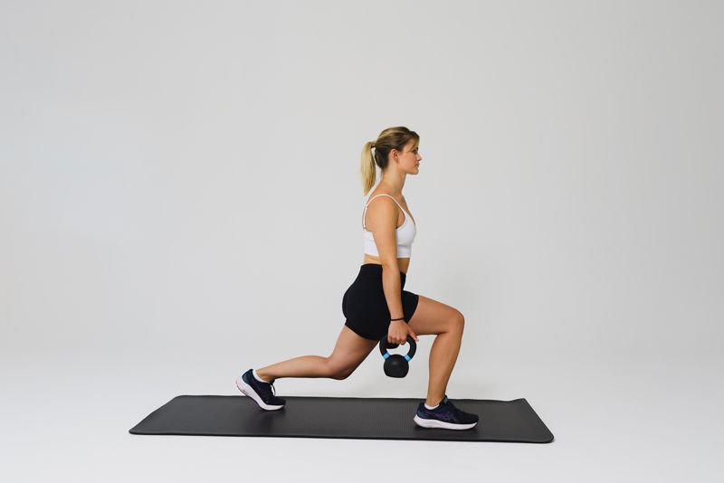 Eine Frau macht Ausfallschritte mit einer Kettlebell auf einer Matte.