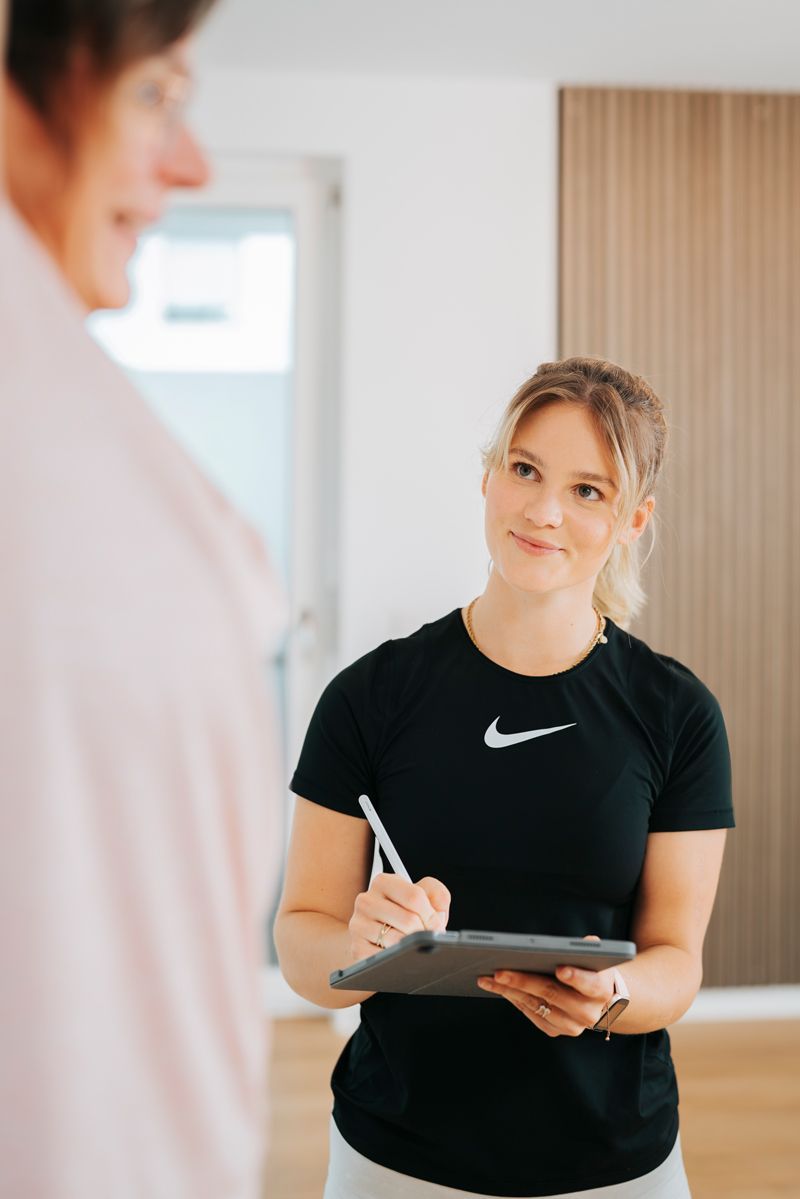 Eine Frau hält ein Klemmbrett und schreibt darauf, während sie mit einer anderen Frau spricht.