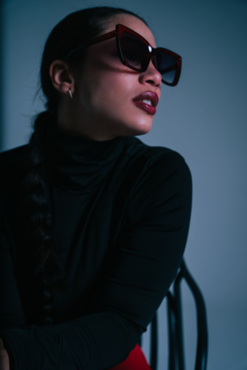 Eine Frau mit Sonnenbrille und schwarzem Rollkragenpullover sitzt auf einem Stuhl.