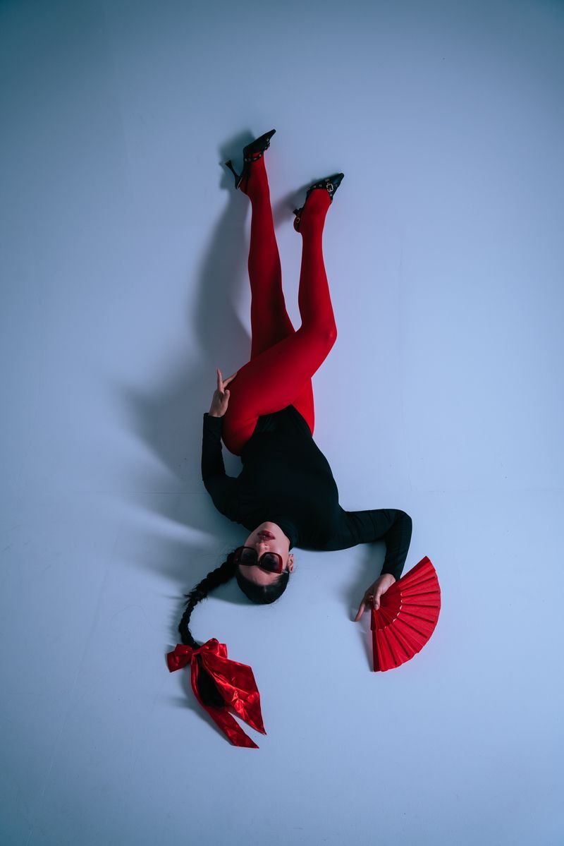 Eine Frau in roten Hosen und Heels steht kopfüber und hält einen roten Fächer