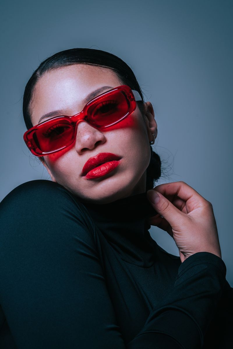 Eine Frau mit roter Sonnenbrille und rotem Lippenstift schaut in die Kamera.