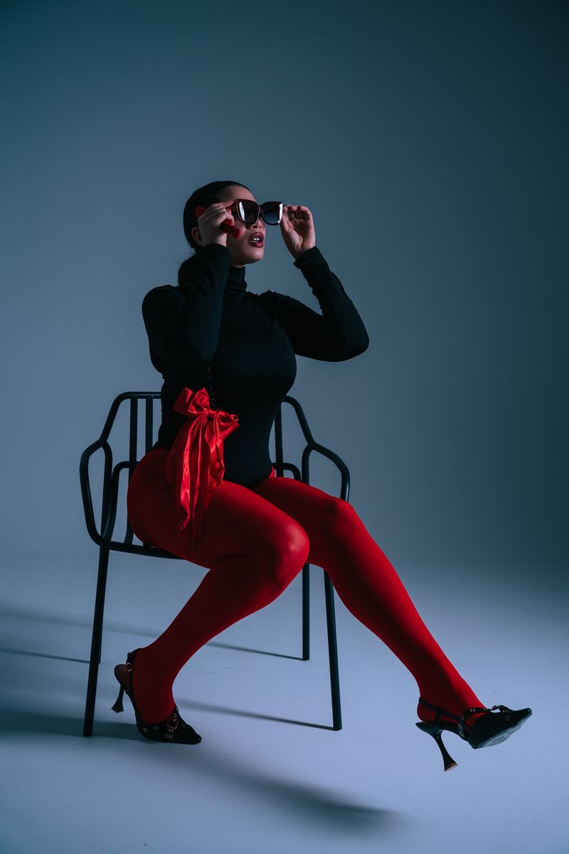 Eine Frau sitzt auf einem Stuhl und trägt rote Strumpfhosen und eine Sonnenbrille.