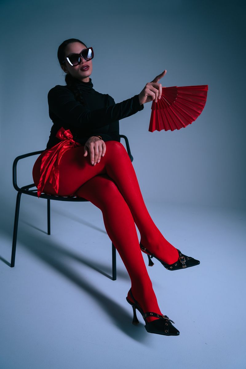 Eine Frau in roten Strumpfhosen sitzt mit einem Fächer in der Hand auf einer Bank.