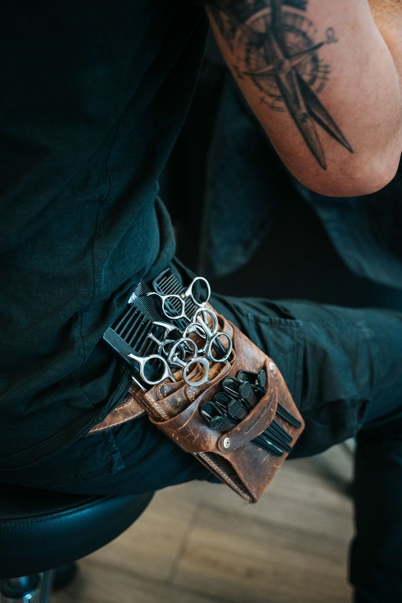 Eine Person mit einer Tätowierung auf dem Arm hält eine Schere und einen Kamm.