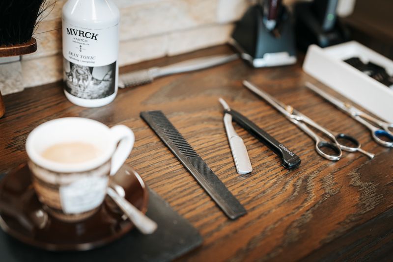 Auf dem Tisch steht eine Tasse Kaffee neben einem Rasiermesser und einer Schere.