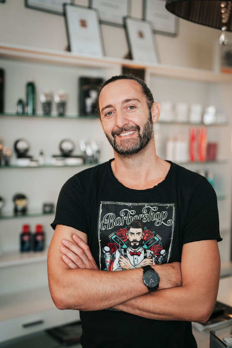 Ein Mann mit Bart steht mit verschränkten Armen in einem Raum.