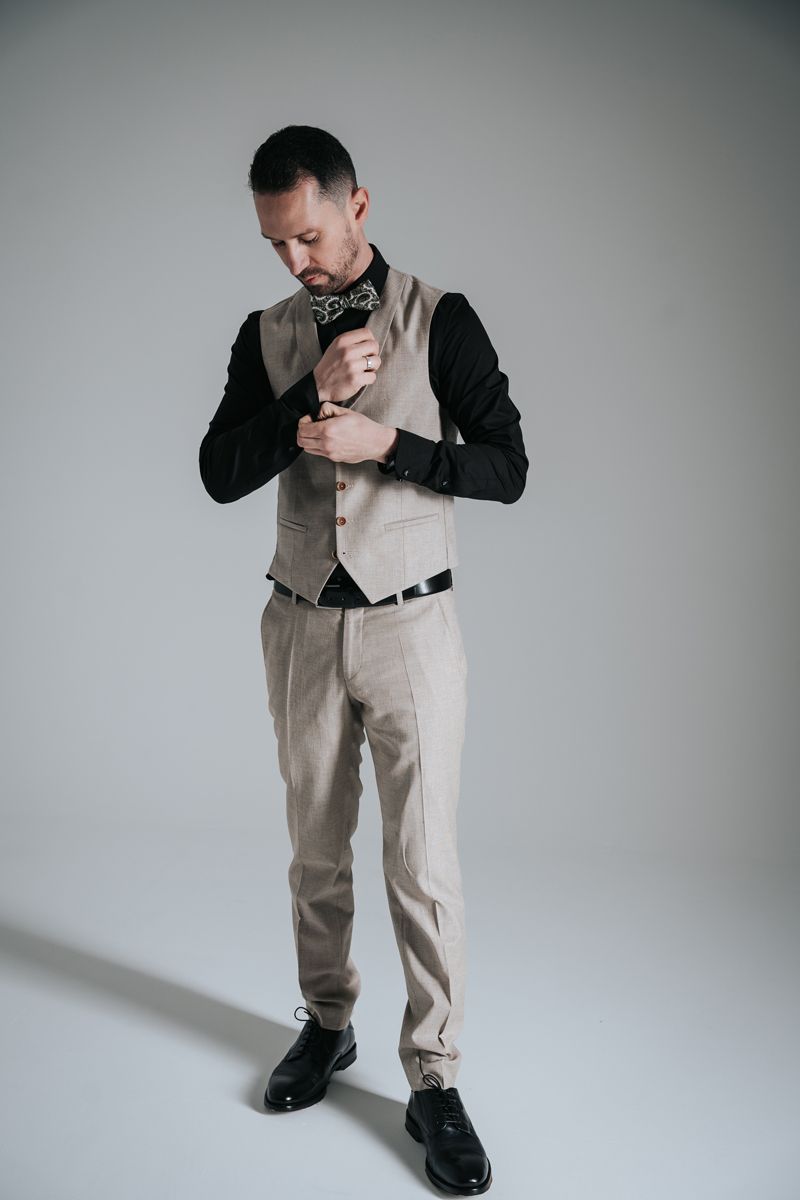 Ein Mann in Anzug und Fliege steht vor einer weißen Wand.