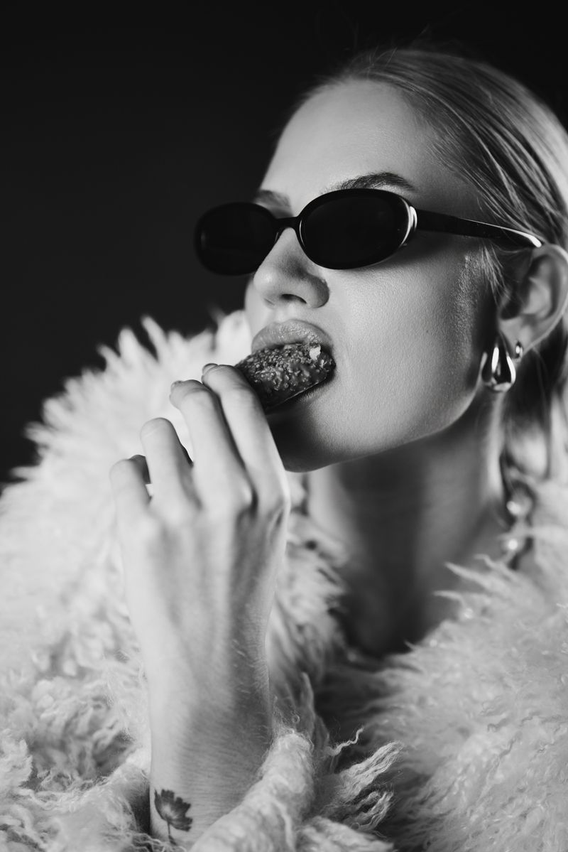 Eine Frau mit Sonnenbrille und Pelzmantel isst eine Erdbeere.