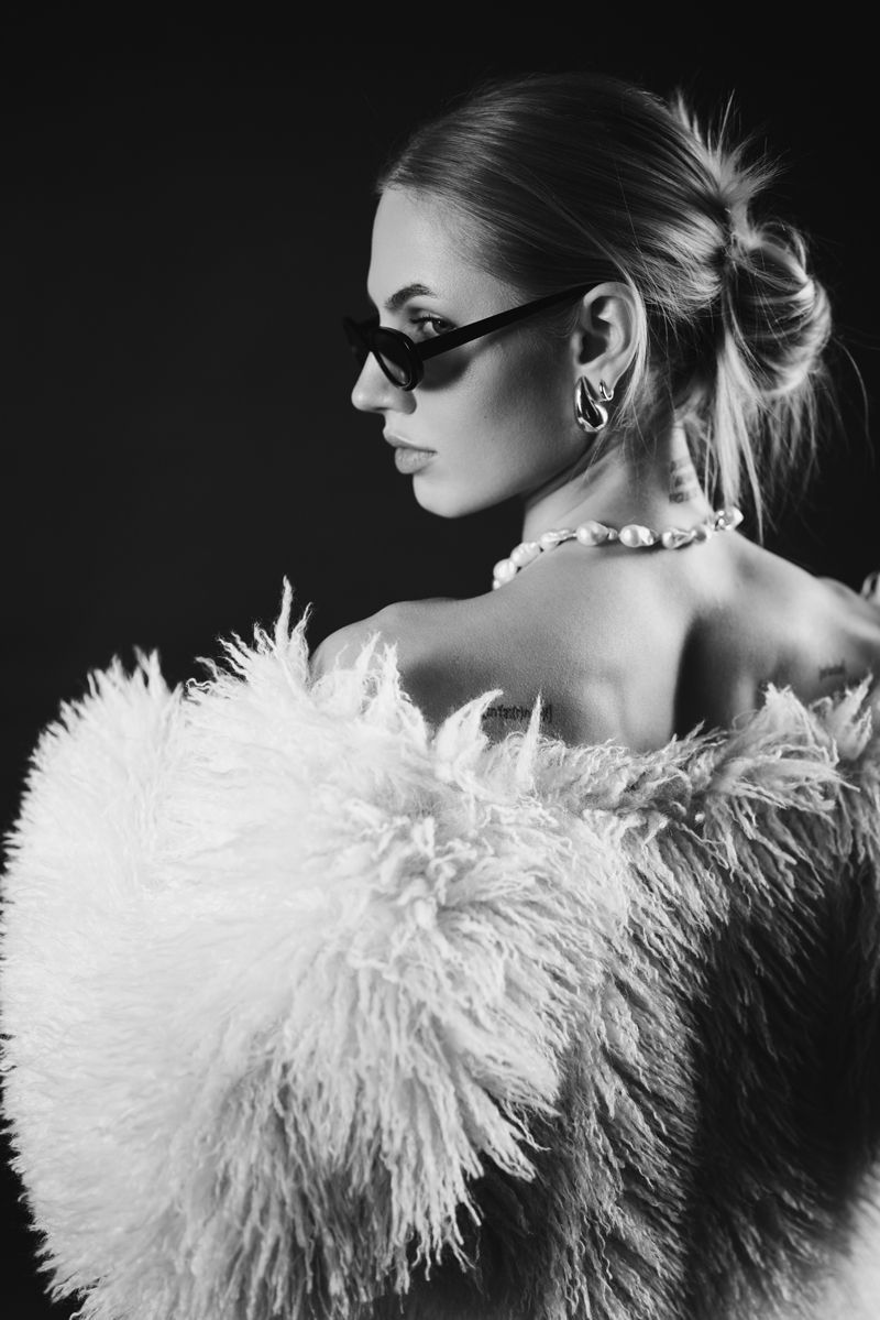 Ein Schwarzweißfoto einer Frau, die einen Pelzmantel und eine Sonnenbrille trägt.