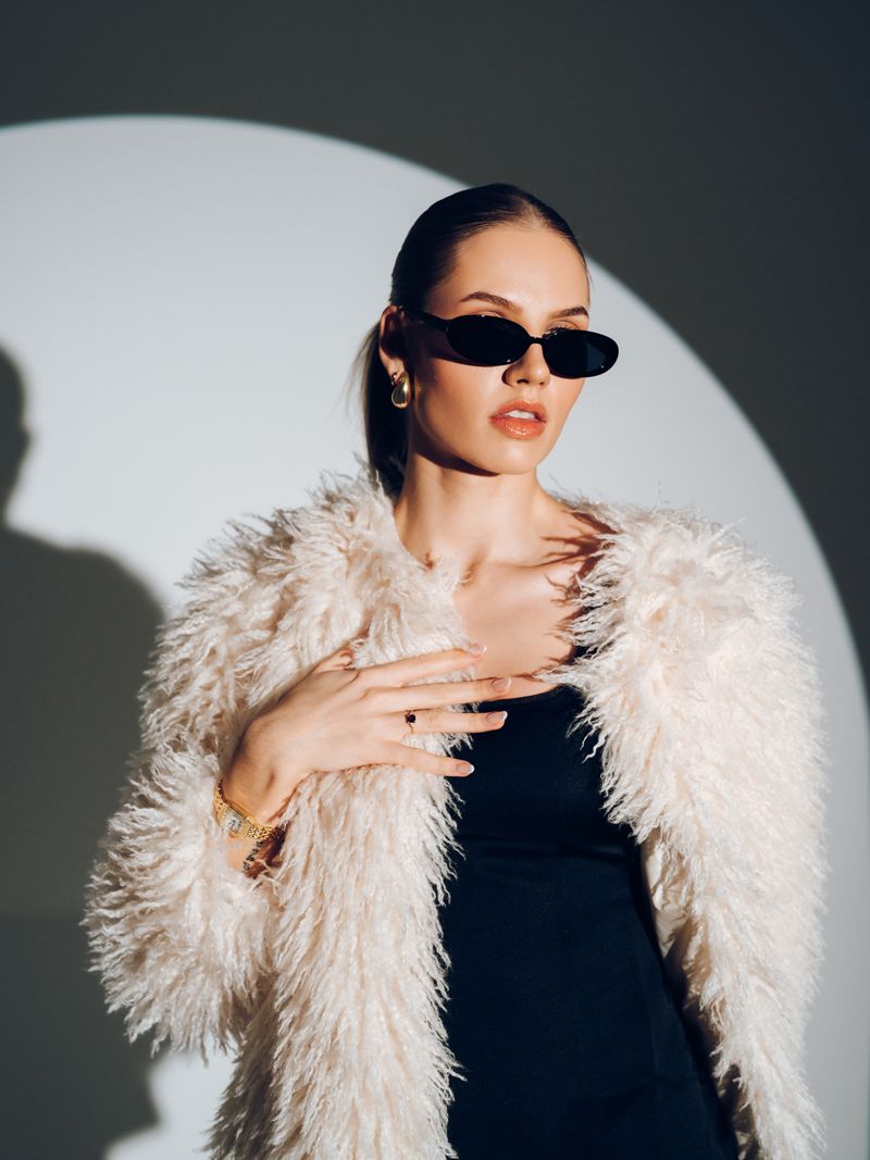 Die Frau trägt eine Sonnenbrille und einen Pelzmantel.