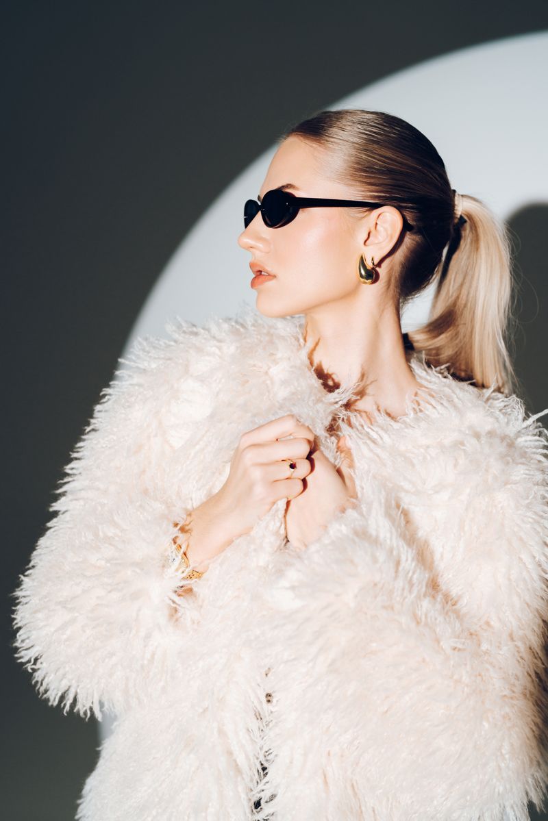 Die Frau trägt einen weißen Pelzmantel und eine Sonnenbrille.