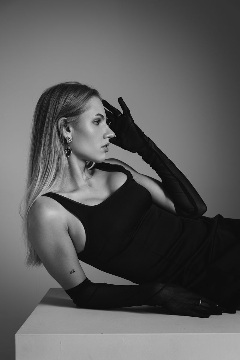 Eine Frau in einem schwarzen Kleid und langen Handschuhen liegt auf einem Tisch.