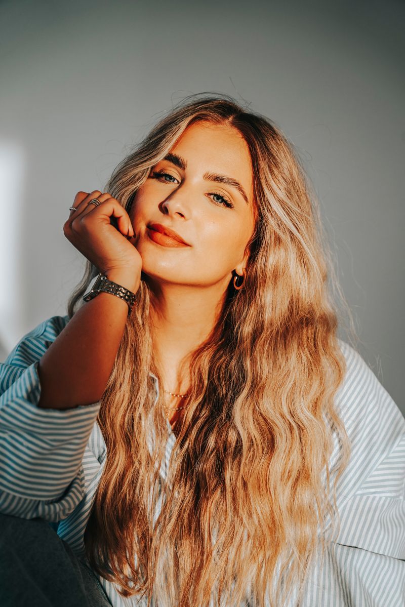 Eine Frau mit langen blonden Haaren trägt ein gestreiftes Hemd und eine Uhr.