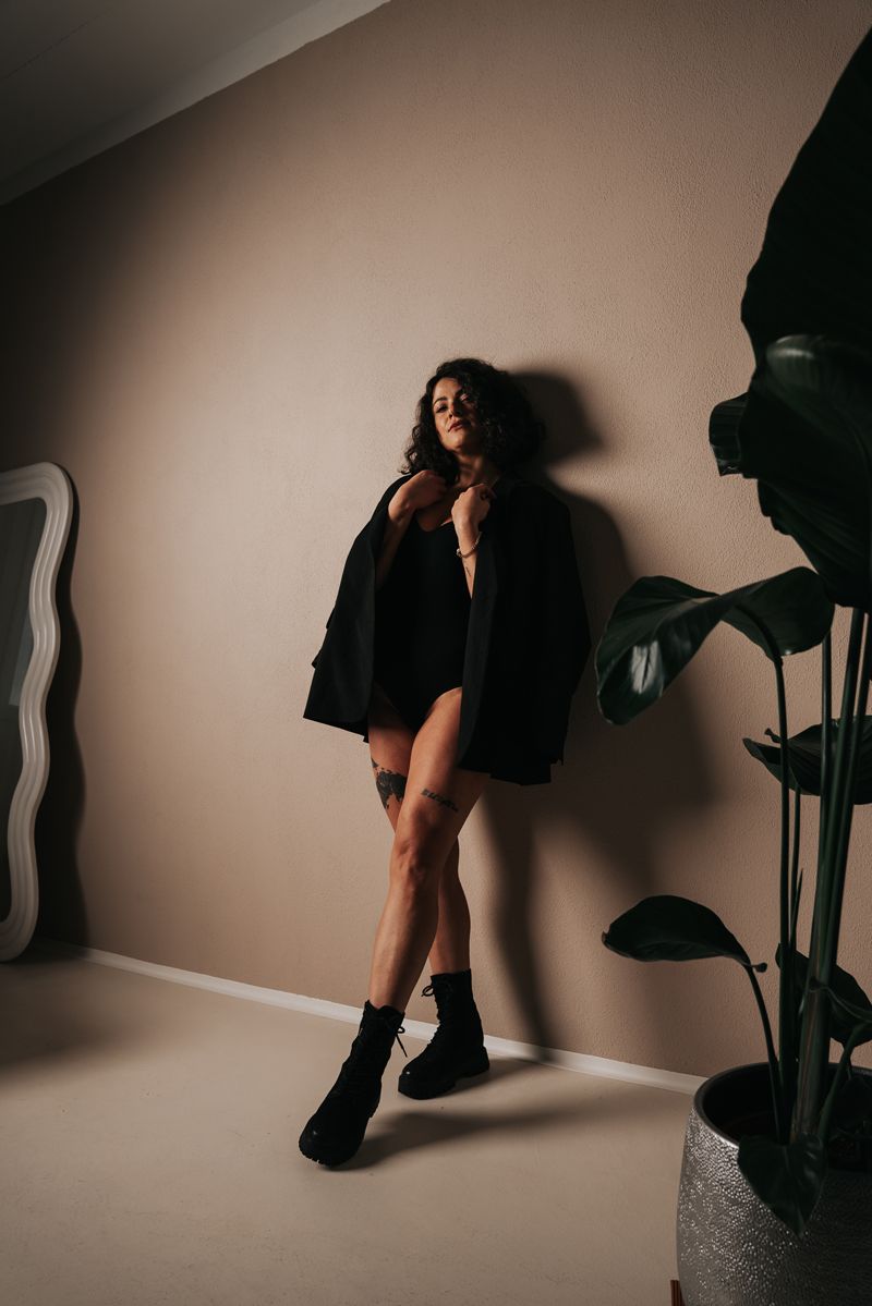 Eine Frau in einer schwarzen Jacke steht neben einer Pflanze in einem Raum.