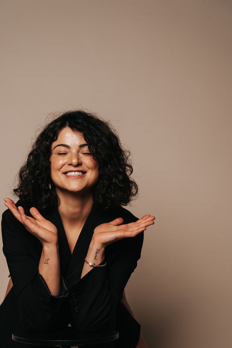 Eine Frau mit lockigem Haar lächelt und erhebt ihre Hände in der Luft.