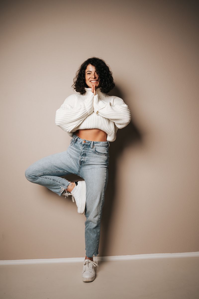 Eine Frau in einem weißen Pullover und Jeans steht auf einem Bein.