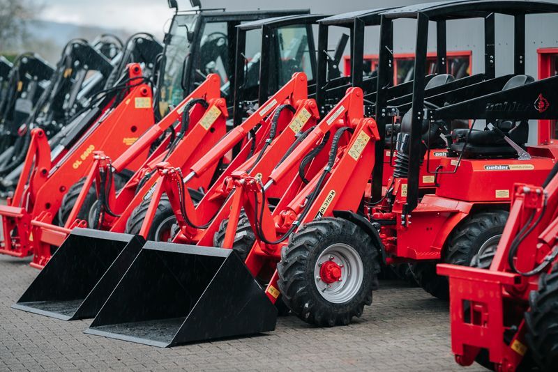 Auf einer Ziegelsteinstraße parken mehrere rote Traktoren nebeneinander in einer Reihe.