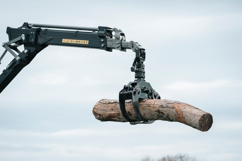 Ein Kran hebt einen Baumstamm in die Luft.