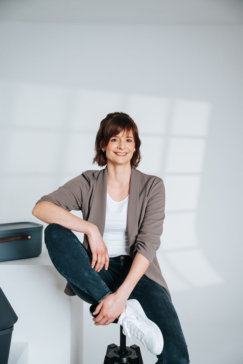 Eine Frau sitzt mit überkreuzten Beinen auf einem Barhocker und lächelt.