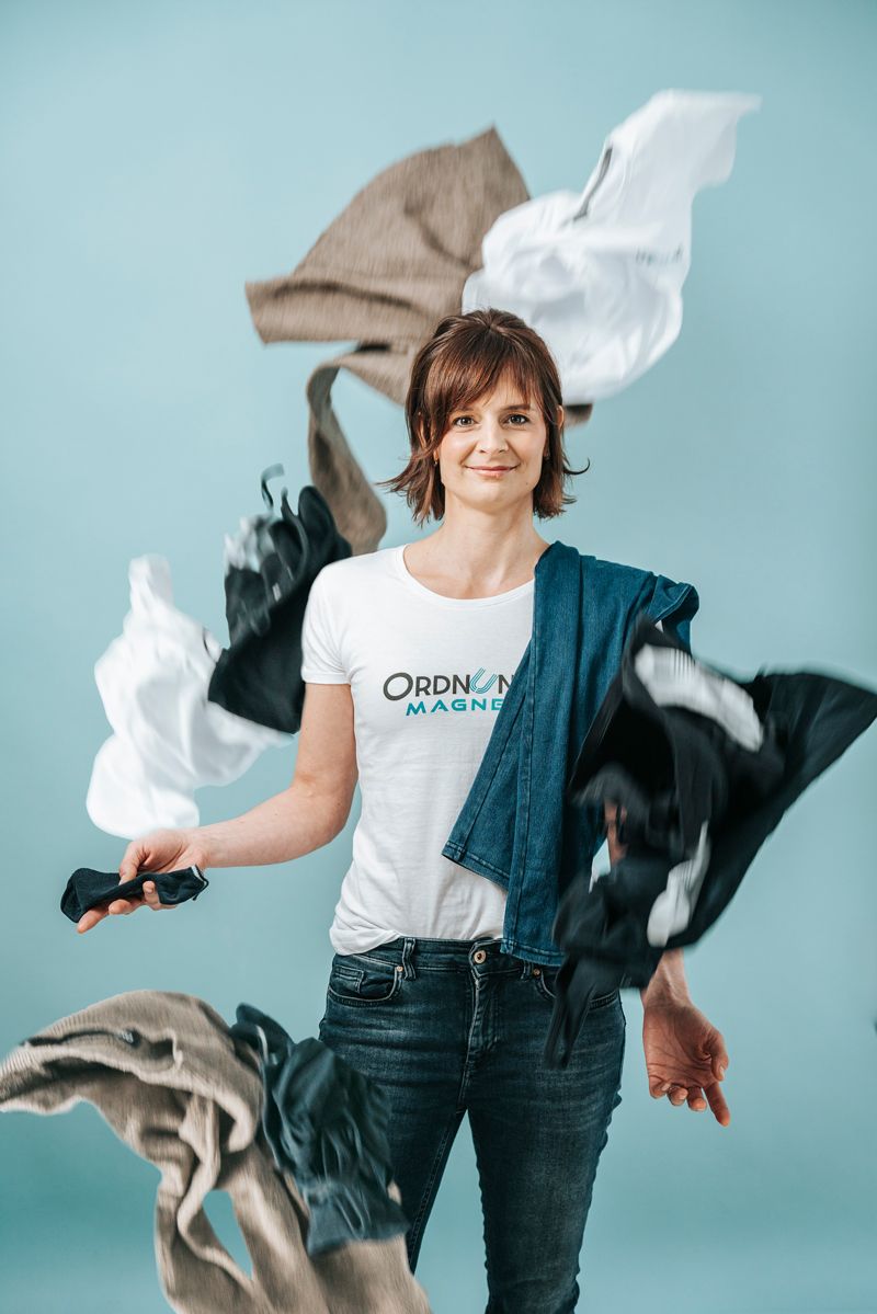 Eine Frau steht vor einem Kleiderstapel.